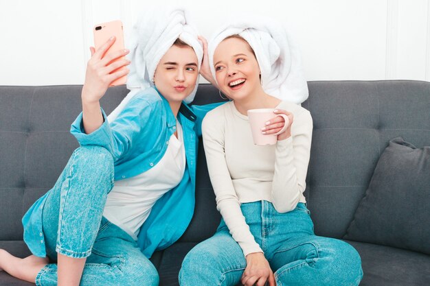 Twee jonge mooie lachende vrouwen zitten op de bank. zorgeloze modellen poseren binnenshuis in een chique appartement of hotelkamer