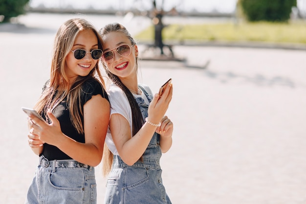Twee jonge mooie meisjes op een wandeling in het park met telefoons. zonnige zomerdag, vreugde en vriendschappen.