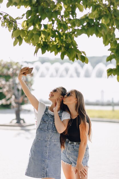 Twee jonge mooie meisjes tijdens een wandeling in het park die foto's van zichzelf aan de telefoon nemen