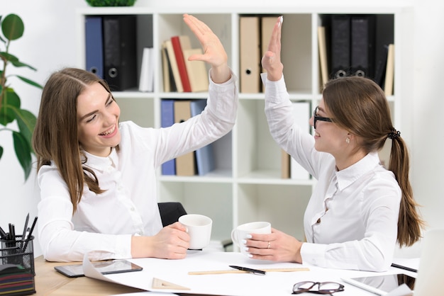 Twee jonge onderneemsters die elkaar bekijken die hoogte vijf aan elkaar in het bureau geven