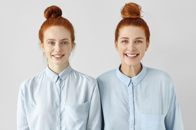 Twee jonge roodharige blanke vrouwen die op elkaar lijken en dezelfde formele lichtblauwe shirts dragen