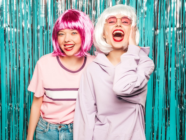 Twee jonge sexy hipster meisjes in pruiken en rode lippen. Mooie trendy vrouwen in zomer kleding plezier