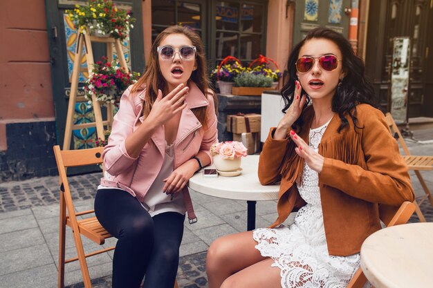 Twee jonge stijlvolle vrouwen zitten in café