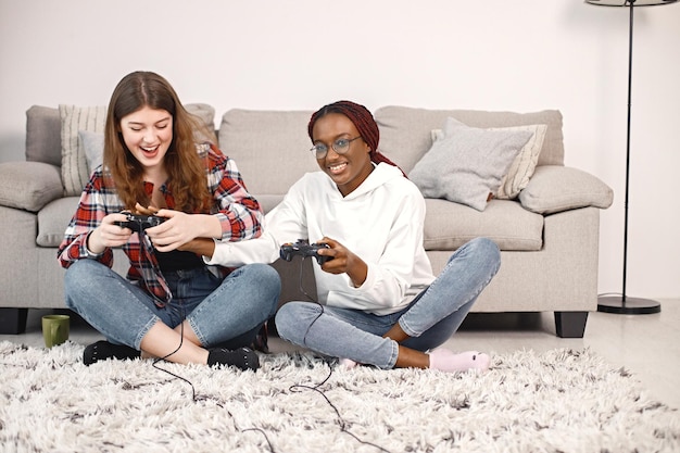 Twee jonge tienermeisjes die op een vloer bij bed zitten en in playstation . spelen