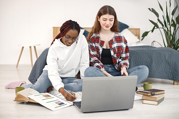 Twee jonge tienermeisjes zittend op een vloer in de buurt van bed studeren en gebruiken een laptop