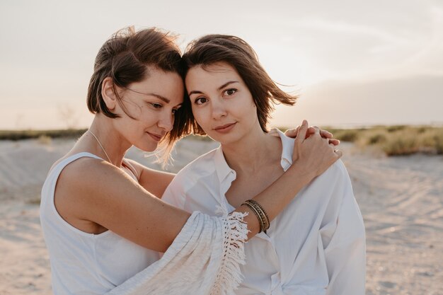 Twee jonge vrouwen die plezier hebben op het zonsondergangstrand, homo lesbische liefde romantiek