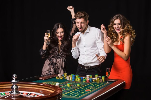 Twee jonge vrouwen en man achter roulettetafel op zwarte achtergrond. Emoties spelers