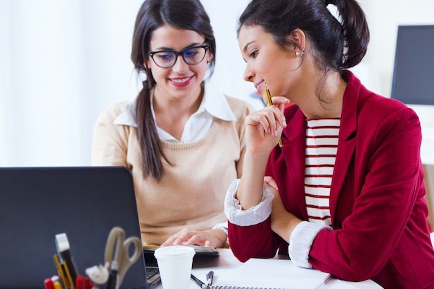 Twee jonge zakenvrouwen werken met laptop in haar kantoor.