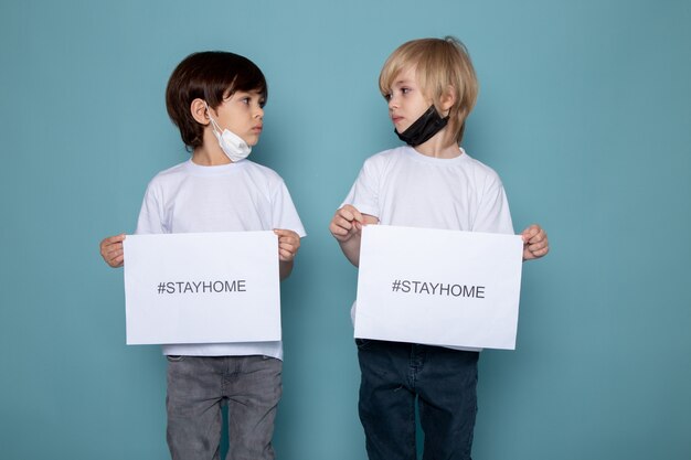 Twee jongens die document met thuis blijven houden hashtag tegen coronavirus op blauw bureau