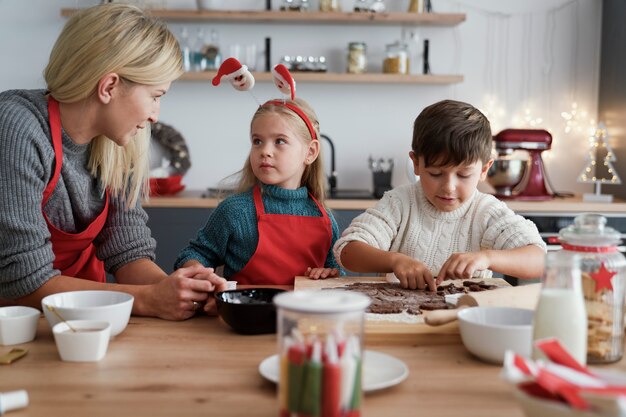 Twee kinderen en hun moeder die peperkoekkoekjes uitsnijden