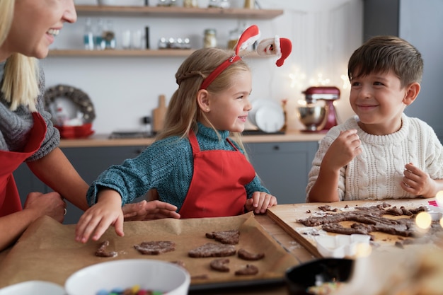 Twee kinderen en hun moeder die peperkoekkoekjes uitsnijden