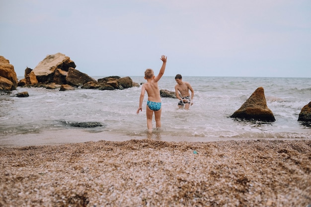 twee kinderen spelen op het strand in de zee tussen de stenen