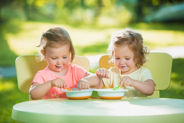 Twee kleine meisjes zitten aan een tafel en samen eten tegen groen gazon