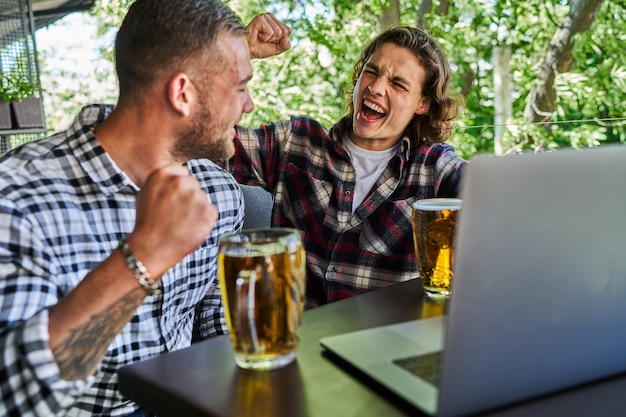 Gratis foto twee knappe mannen voetbal kijken in een pub en bier drinken.