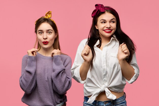 Twee knappe, modieuze jonge vriendinnen, stijlvol gekleed in een goed humeur, glimlachend en lachend, opgewonden met geweldig nieuws