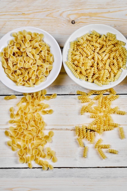 Gratis foto twee kommen ongekookte pasta's op houten tafel.