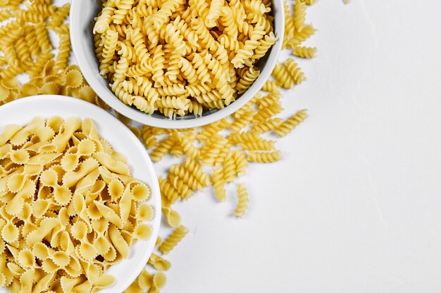 Twee kommen ongekookte pasta's op witte achtergrond