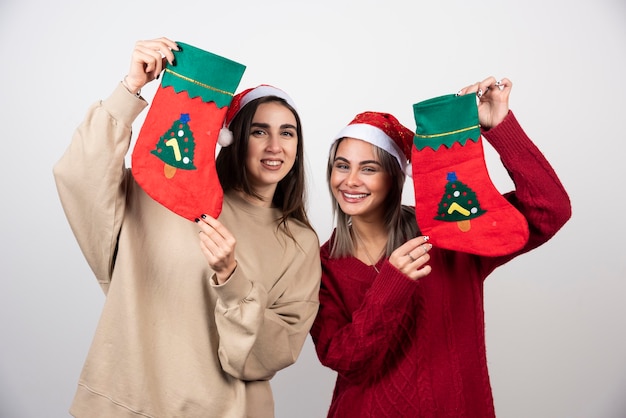 Twee lachende meisjes in kerstmuts met kerstsokken.