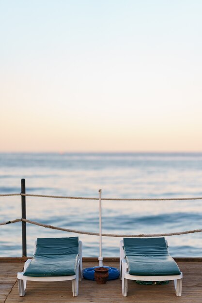 Twee lege sinbeds op houten pier op mooie rustige ochtend. Toeristische werf in de baai van zee