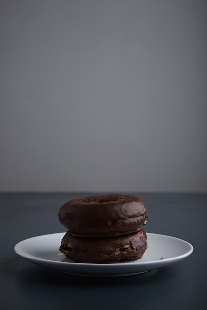 Twee lekkere vers gebakken donuts geglazuurd met chocolade op witte keramische plaatje geïsoleerd op rustieke oude blauwe houten tafel. zijaanzicht