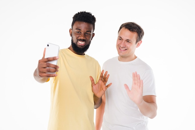 Twee mannen van gemengd ras die selfie met smartphonecamera nemen die op witte muur wordt geïsoleerd