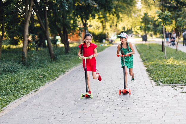 Twee meisjes die berijdende duwautoped in het park genieten van