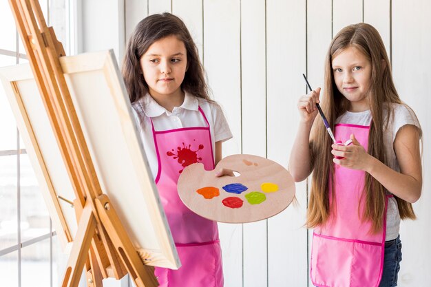 Twee meisjes die het roze schort schilderen samen op schildersezel dragen