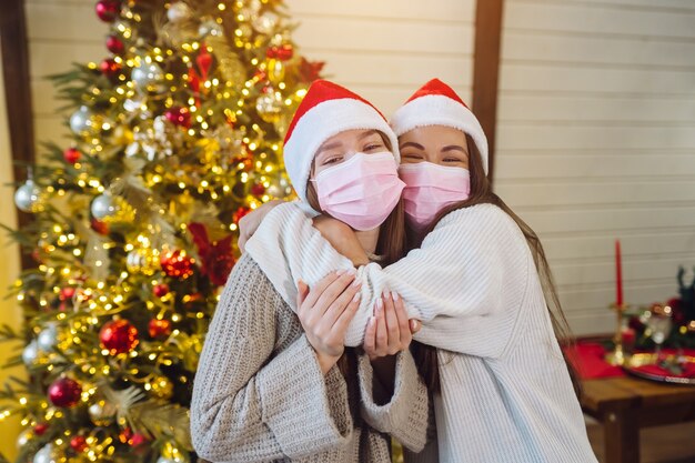 Twee meisjes die in beschermende maskers de camera bekijken. Kerstmis tijdens coronavirus, concept