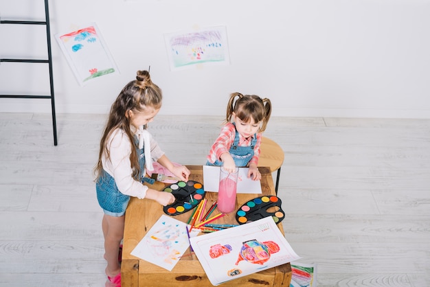 Twee meisjes die met aquarelle bij houten lijst schilderen