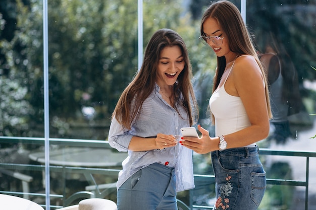 Twee meisjes die telefoon in een koffie gebruiken