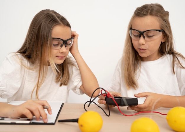 Gratis foto twee meisjes doen wetenschappelijke experimenten met citroenen en elektriciteit