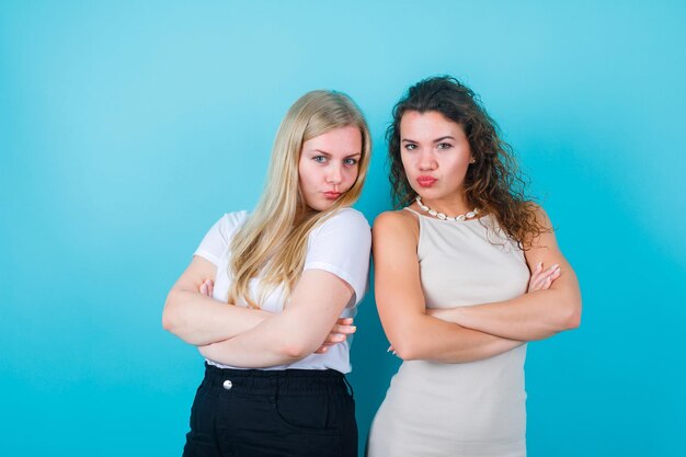 Twee meisjes kijken naar de camera door hun armen over elkaar te kruisen op een blauwe achtergrond