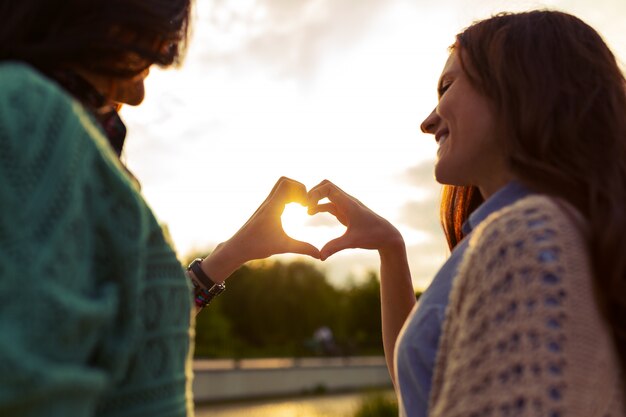 Twee meisjes tonen hart uit handen bij zonsondergang