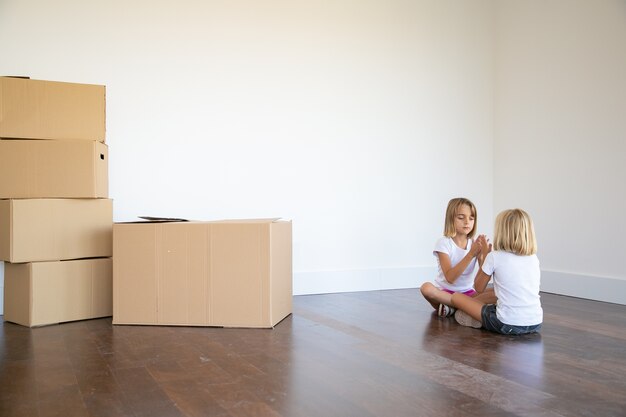 Twee meisjes zittend op de vloer in de buurt van hoop dozen in hun nieuwe appartement en samen spelen