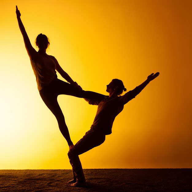 Twee mensen die yoga in het zonsonderganglicht uitoefenen