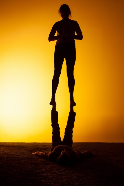 Gratis foto twee mensen die yoga in het zonsonderganglicht uitoefenen