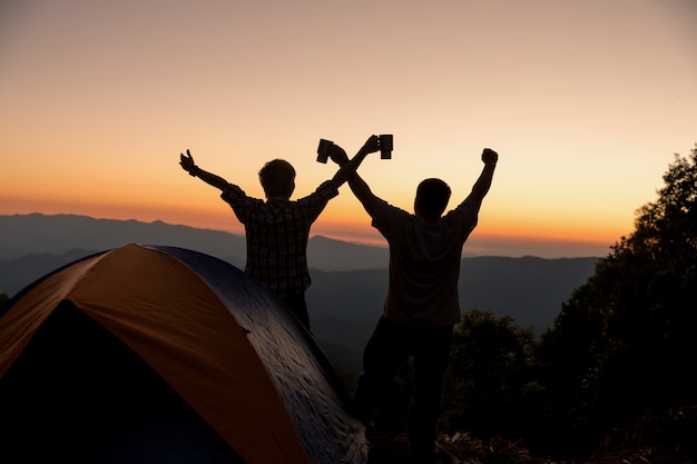 Twee mensentoeristen gelukkig op de bovenkant van de berg bij dichtbijgelegen kampvuur