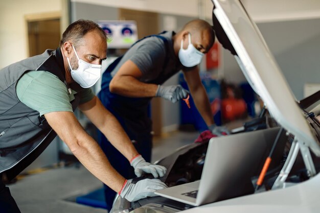 Twee monteurs die een beschermend gezichtsmasker dragen tijdens het repareren van de automotor in een werkplaats