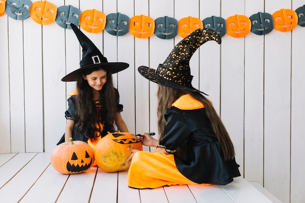 Gratis foto twee mooie halloween-heksen die pompoenen schilderen