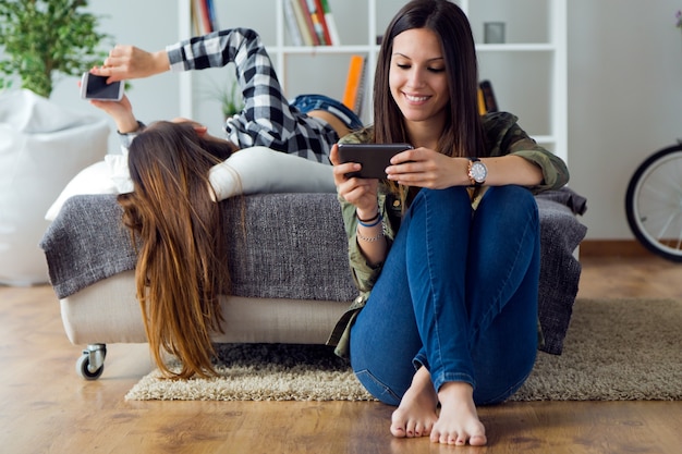 Twee mooie jonge vrouw met behulp van mobiele telefoon thuis.