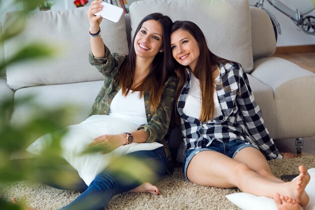 Twee mooie jonge vrouw met behulp van mobiele telefoon thuis.