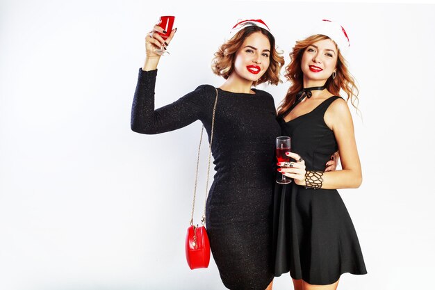 Twee mooie sexy meisjes in rode kerst kerstman vakantie hoed poseren op witte achtergrond, met glas wijn.