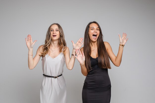 Twee mooie vrouwen die in de studio staan en hun vingers naar boven wijzen, geïsoleerd op een grijze achtergrond