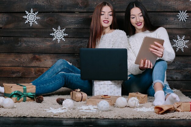 Twee mooie vrouwen die op de vloer met laptop en tablet, tussen giften voor Kerstmis aanbrengen