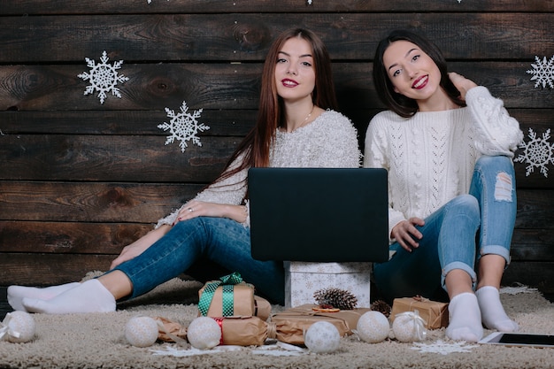 Twee mooie vrouwen liggen met een laptop op de grond tussen kerstcadeautjes