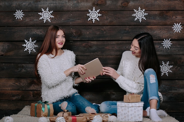 Twee mooie vrouwen zittend op de vloer met een tablet, tussen cadeaus voor Kerstmis