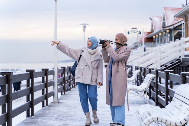 Gratis foto twee moslim vriendinnen wandelen langs de oceaan en nemen foto's tijdens het reizen