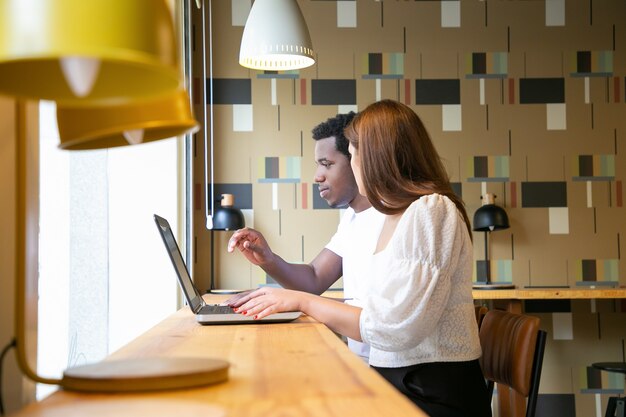 Twee multi-etnische ontwerpers zitten samen en werken op laptop in coworking space