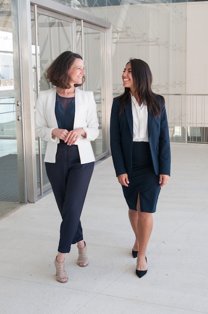 Gratis foto twee ontspannen vrouwelijke collega's die in bureauzaal lopen