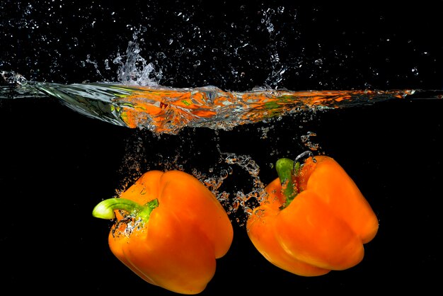 Twee oranje groene paprika die onder het water drijft